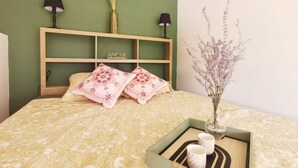 Un letto rifatto con cura, una comodino con due lampade, un vaso decorativo con fiori secchi e un vassoio con due tazze.