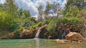 Paesaggio naturale con cascata, acqua limpida e vegetazione circostante.