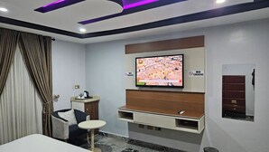 A modern hotel room with a flat-screen TV mounted on the wall, a small table, a sofa, and a cabinet with a mirror. - De Don's Villa (Abuja)