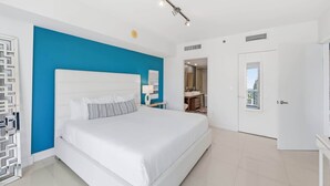 Ein modernes Schlafzimmer mit einem großen Bett, einer blauen Akzentwand, einem weißen Kopfteil und Blick auf die Stadt durch eine Tür.
