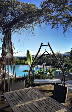 Eine Holzterrasse mit einer Schaukel, einem Hängesessel und Blick auf ein Schwimmbad und Berge.