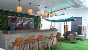 A bar area with wooden stools, a green artificial turf floor, and hanging pendant lights. - Qlets Prive's Shortlets (Abuja)