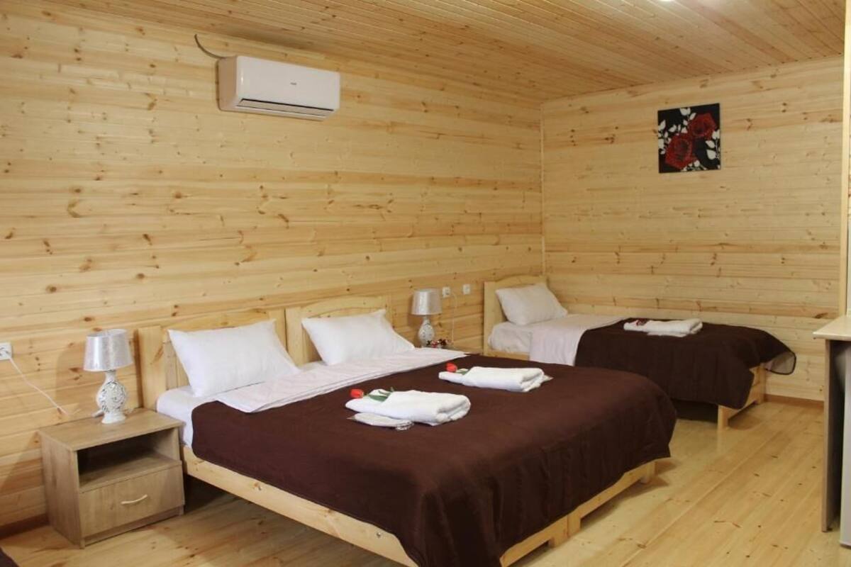 A wooden cabin room with two beds, a nightstand, an air conditioning unit, and a wall-mounted artwork.