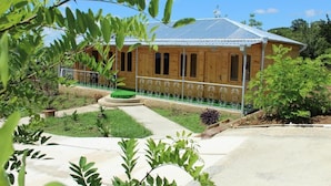 A wooden house with a metal roof, surrounded by greenery and a paved area. - GREEN VILLA TSKALTUBO (Tsqaltubo)