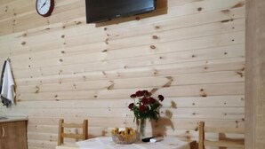 A wooden interior with a dining table, chairs, a clock, and a flat-screen TV mounted on the wall. - GREEN VILLA TSKALTUBO (Tsqaltubo)