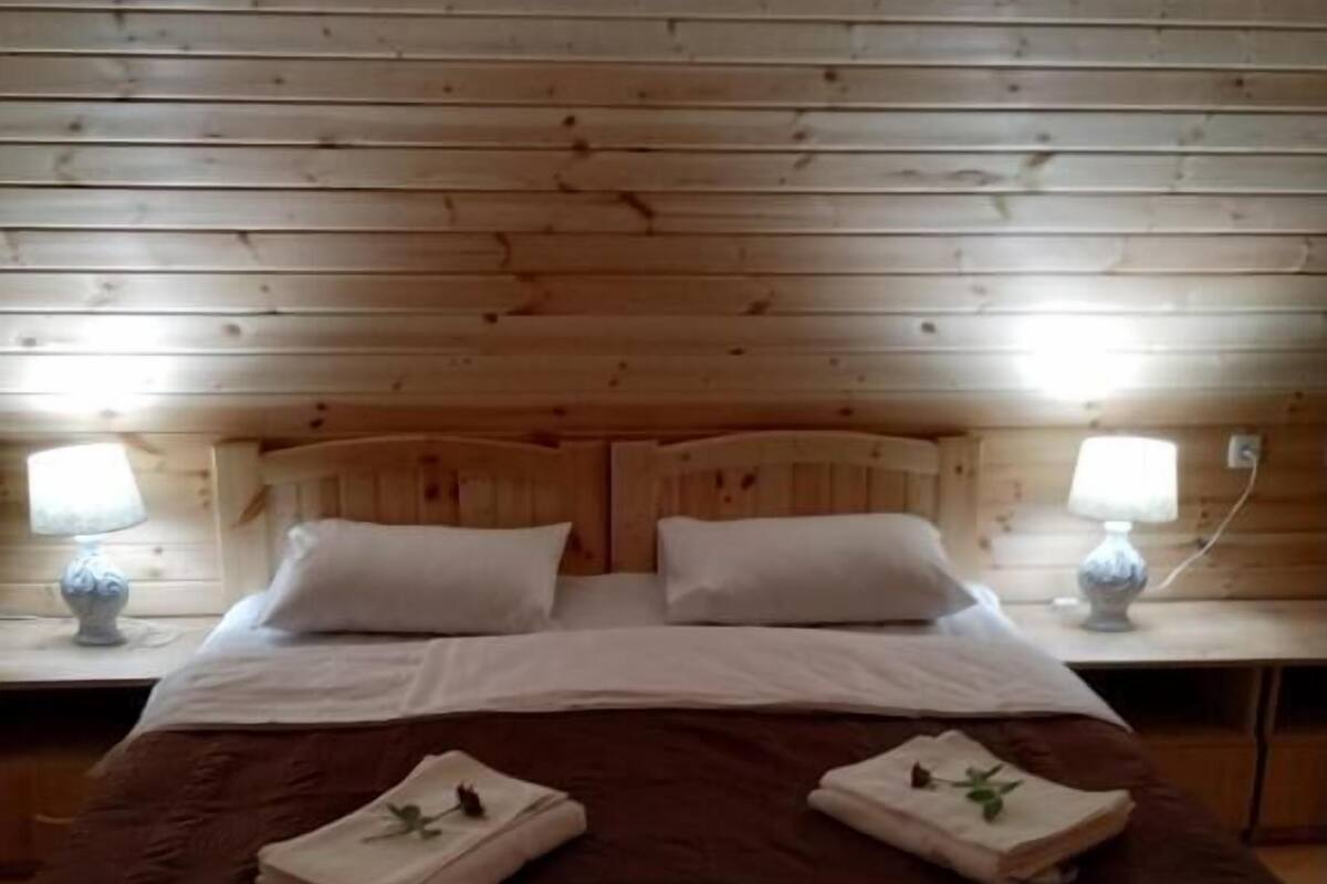 A wooden-paneled room with a bed, two bedside lamps, and an air conditioning unit.