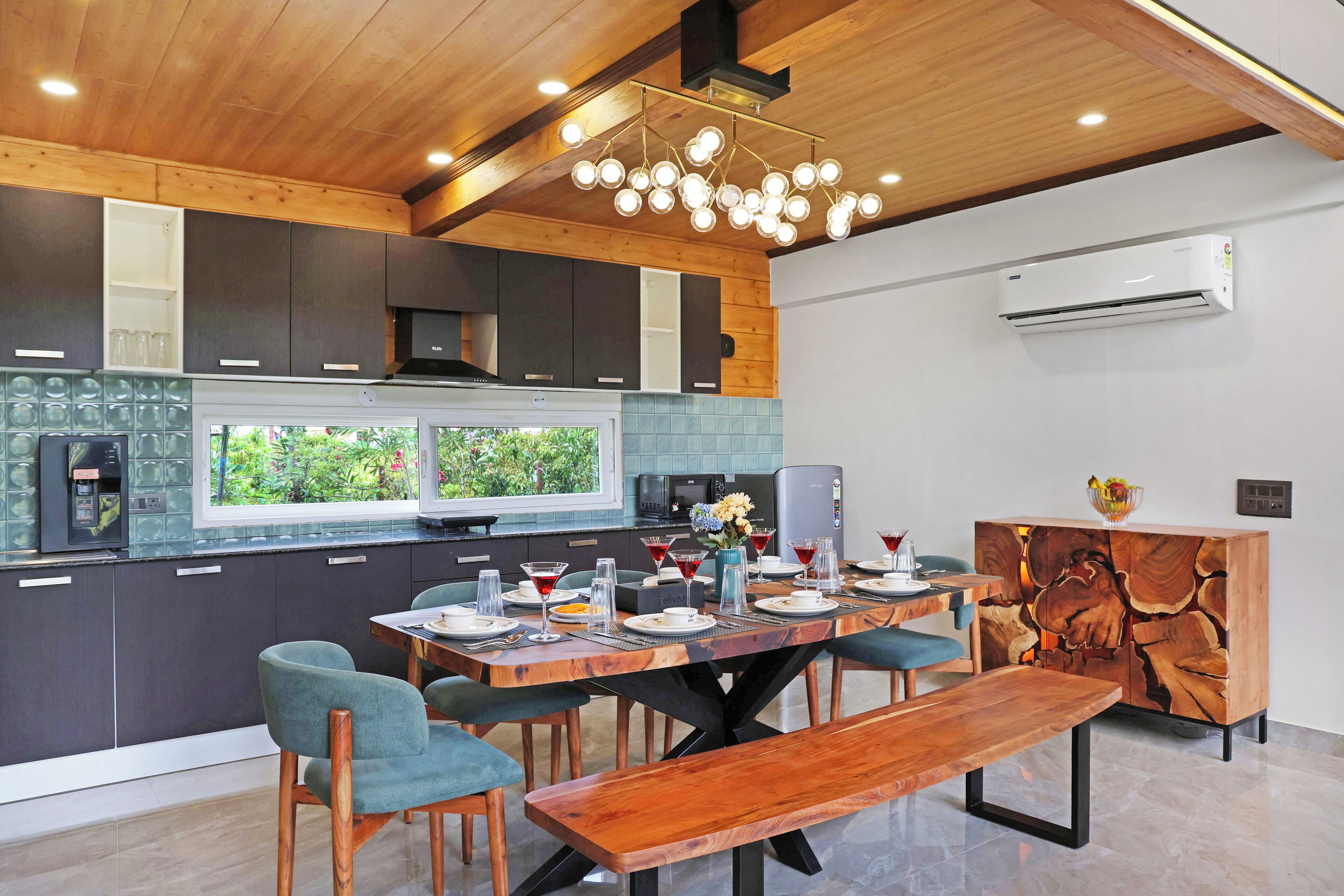 A modern kitchen with dark cabinets, a wooden ceiling, and a dining area with a wooden table and chairs.
