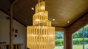 A modern interior with a large chandelier, wooden beams, and a view of the outdoors. - ELIVAAS Esh Cottages (Palampur)