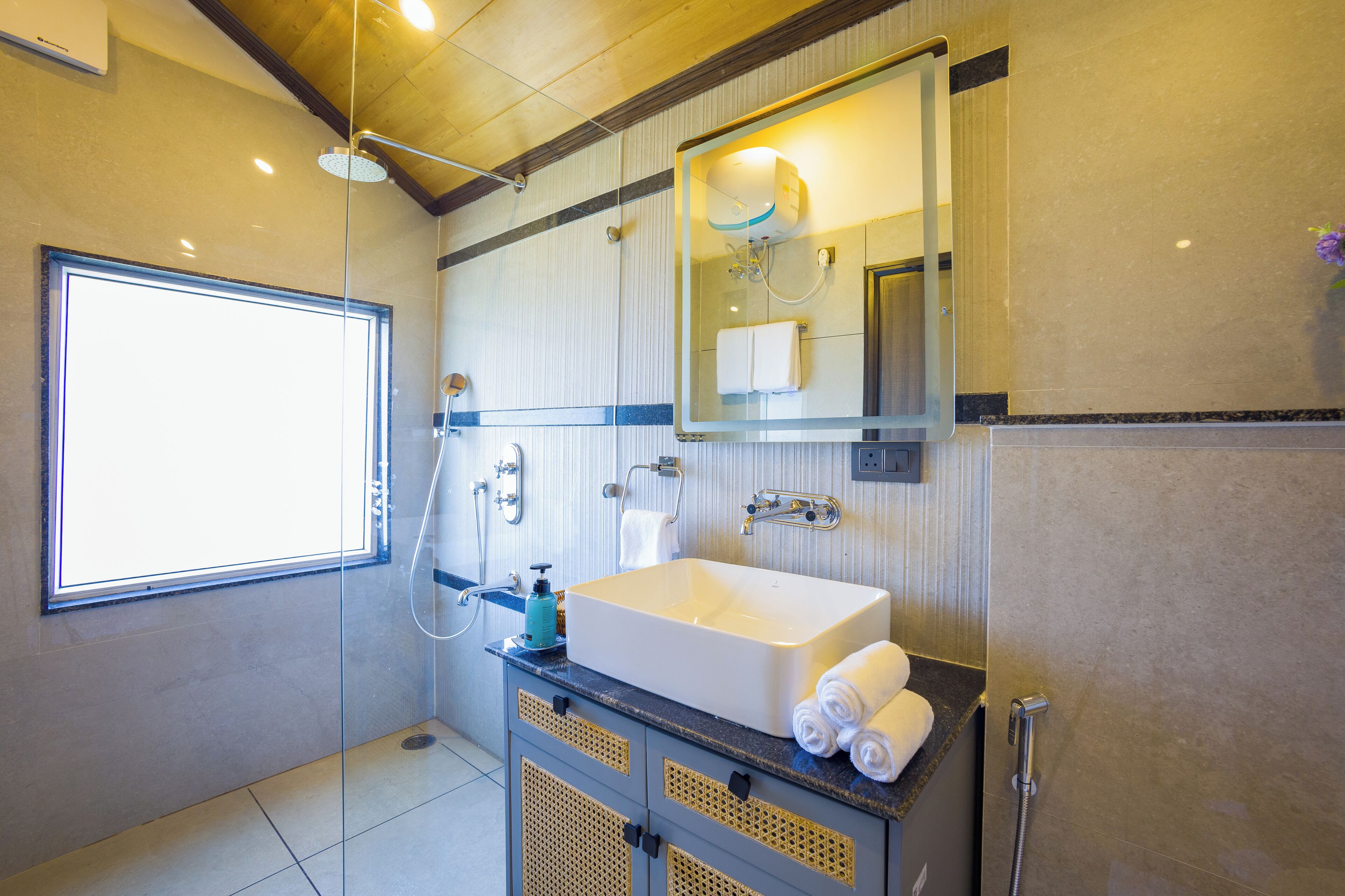 Un baño moderno con un ventanal grande, cabina de ducha de vidrio, lavamanos blanco y un espejo sobre él.