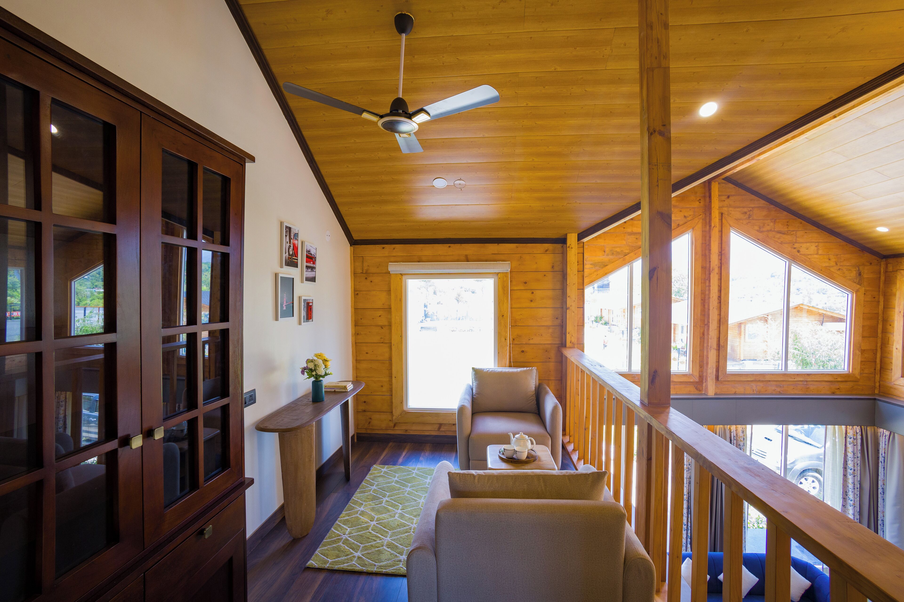 Interior acogedor de una cabaña con techo de madera, zona de comedor con mesa y sillas, y amplios ventanales con vistas al exterior.