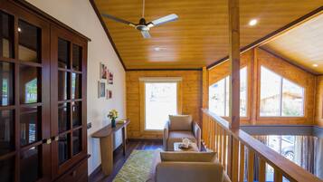 Interior acogedor de una cabaña con techo de madera, zona de comedor con mesa y sillas, y amplios ventanales con vistas al exterior.