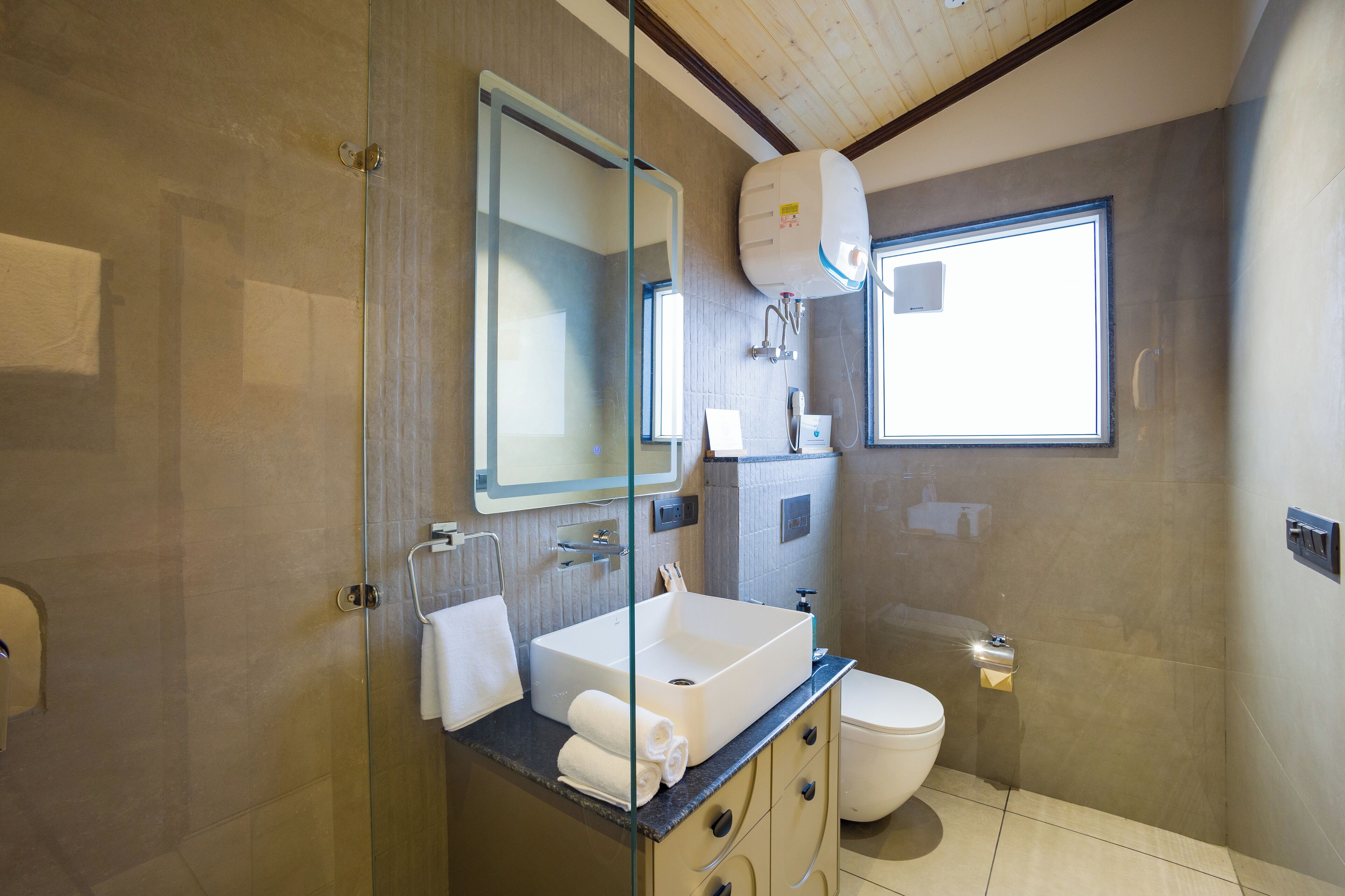 A modern bathroom with a glass shower enclosure, a large mirror, a built-in sink, and a toilet.