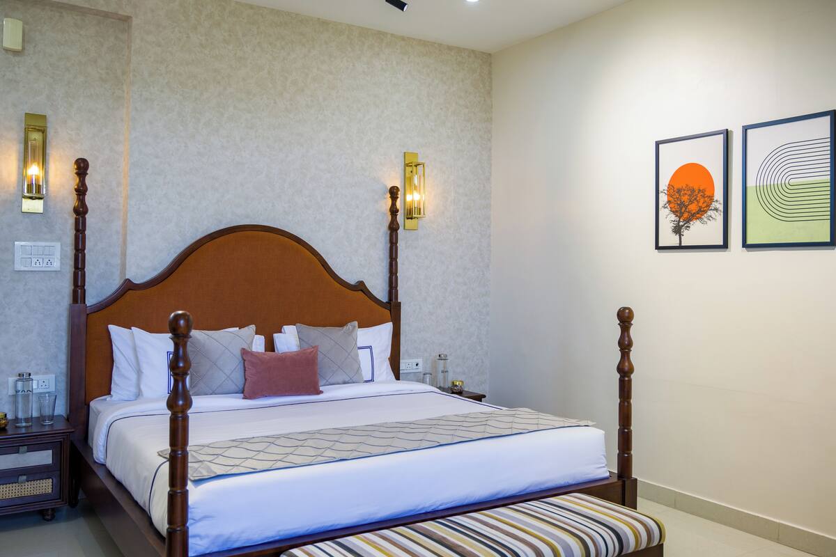 A neatly made bed with a wooden headboard, a bedside table with a lamp, and two framed artworks on the wall.