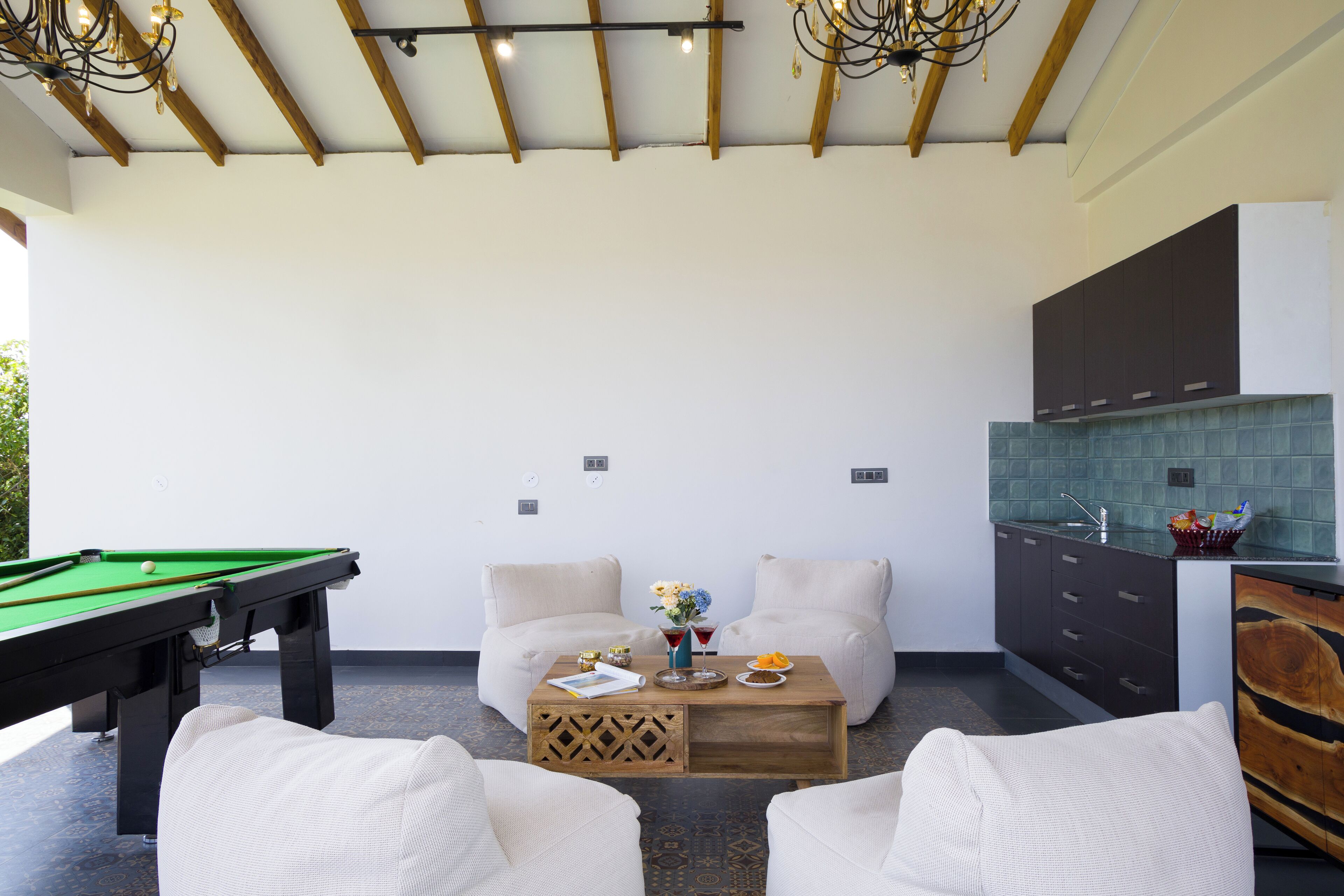 A pool table, two sofas, a coffee table, and a kitchen area with cabinets and a tiled backsplash.