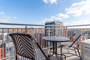 A balcony with two chairs and a table, overlooking a cityscape with modern buildings. - Two-level Apartment in Center | Pool | Gym | Sauna (Gdańsk)