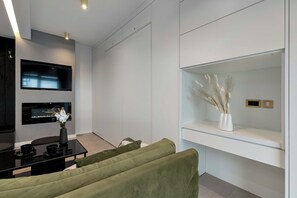 A close-up of the living room's media center, featuring a mounted flat-screen TV above an electric fireplace. The white built-in shelving provides a clean and uncluttered look. - Two-level Apartment in Center | Pool | Gym | Sauna (Gdańsk)