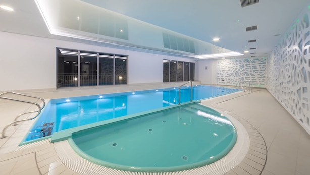 Piscina interna com água azul cristalina, rodeada por piso e paredes azulejadas.