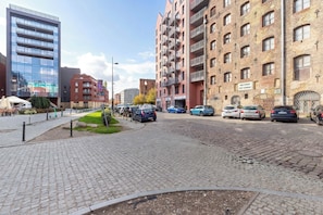 A cobblestone street with modern and traditional buildings, a clear sky, and parked cars. - Two-level Apartment in Center | Pool | Gym | Sauna (Gdańsk)