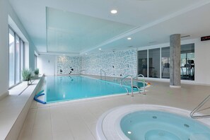 An indoor swimming pool with a separate hot tub area, clear glass walls, and a tiled floor. - Two-level Apartment in Center | Pool | Gym | Sauna (Gdańsk)