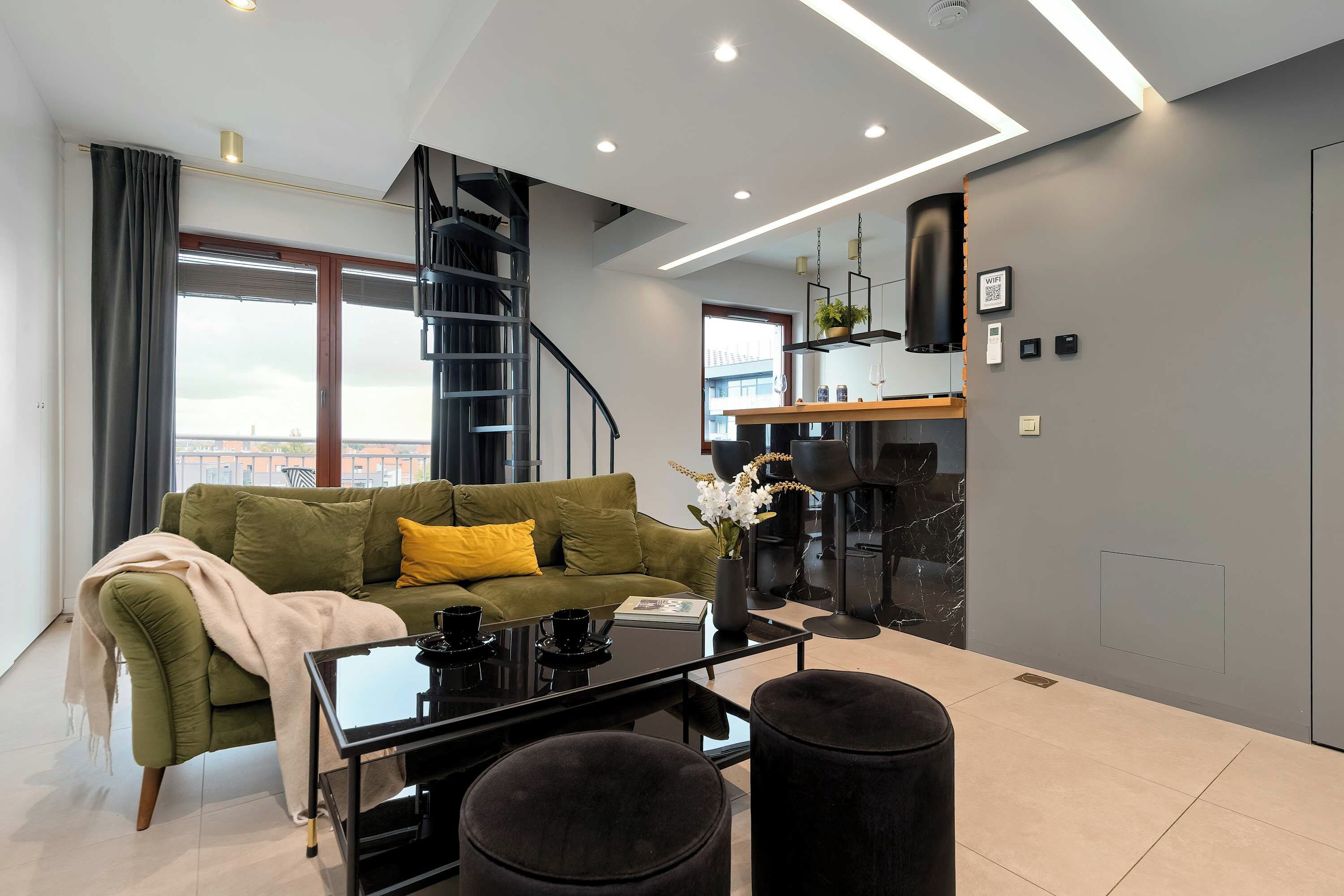 Una sala de estar moderna con un sofá verde, una mesa de centro y una escalera que sube a un nivel superior.