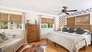Un dormitorio con una cama, un aparador de madera, un ventilador de techo y una ventana con vistas al exterior.