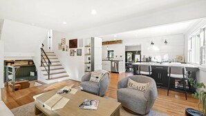 Un espacio habitable espacioso con una escalera de madera, una cocina con isla central y un comedor.
