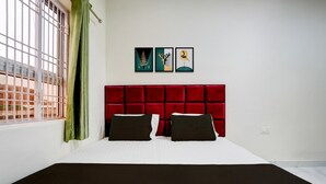 A hotel room with a red headboard, two black pillows, a white bedspread, and a black throw. There are three framed artworks on the wall.