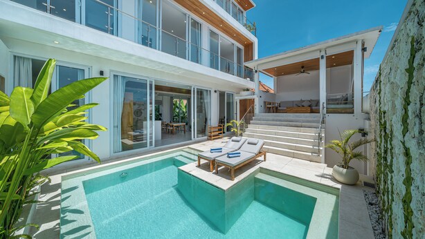 Et moderne hus med to etager, en swimmingpool, udendørs siddepladser og en trappe op til øverste etage.