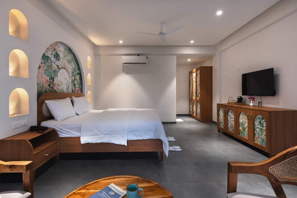 A modern hotel room with a large bed, a wooden nightstand, a desk with a chair, a television, and a cabinet with decorative glass doors.