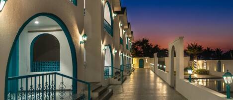 A hotel corridor with a staircase, arched doorways, and exterior lighting.