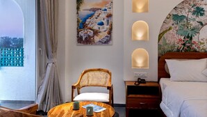 Une chambre d’hôtel avec un lit, une chaise en bois, une petite table avec une tasse et un menu, un tableau représentant un paysage côtier, et trois lampes fixées au mur.
