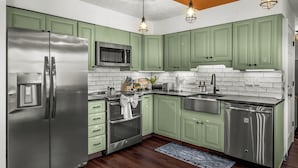 Una cocina moderna con gabinetes verdes, electrodomésticos de acero inoxidable y piso de madera.