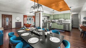 Una cocina moderna con armarios verdes, electrodomésticos de acero inoxidable y un comedor con mesa de madera oscura para seis personas.