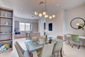 Una cocina moderna con una isla central, un comedor con mesa de vidrio y un espacio de trabajo con escritorio y silla.
