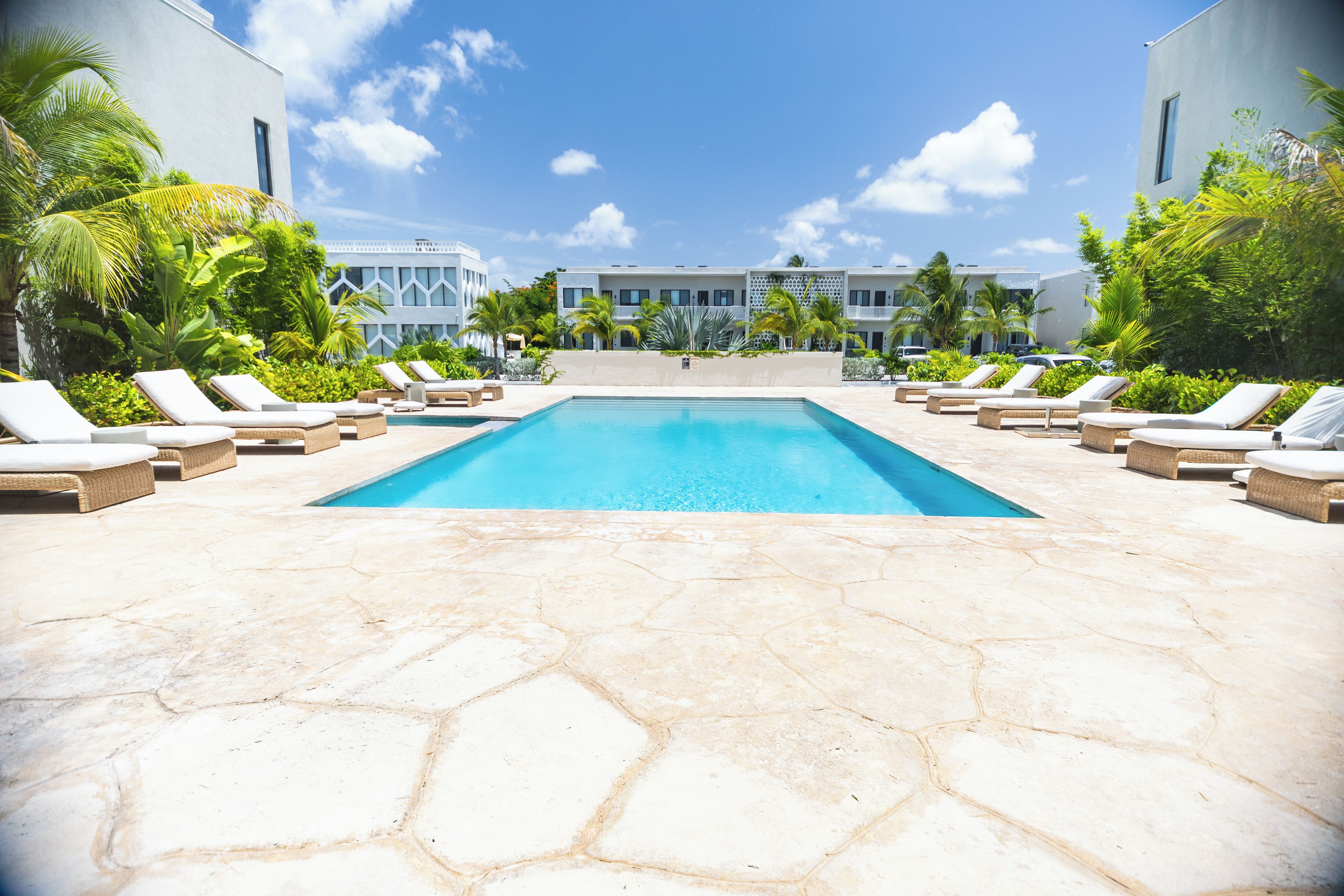 A swimming pool with lounge chairs and palm trees, surrounded by modern buildings.