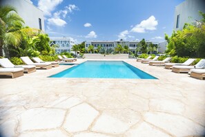 A swimming pool with lounge chairs and palm trees, surrounded by modern buildings. - Modern condo in gated community. Steps to beach. (Nassau)
