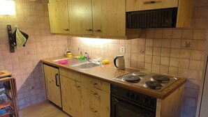 A compact kitchen with wooden cabinets, a sink, a stove, and a microwave. - Lake view Chalet  , Därligen (Interlaken-Oberhasli)
