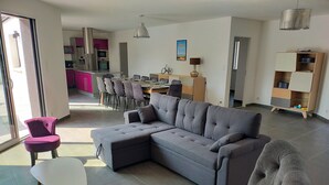 A modern living room with a grey sectional sofa, a small white table, and a purple chair. There is a dining area in the background with a kitchen visible. - Villa near Les Sables d'Olonne with private pool 15 minutes from the beaches! (Saint-Mathurin)