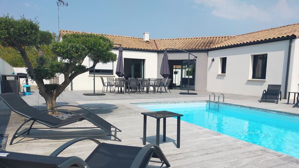 A poolside area with lounge chairs, a small table, and a building with a tiled roof. - Villa near Les Sables d'Olonne with private pool 15 minutes from the beaches! (Saint-Mathurin)