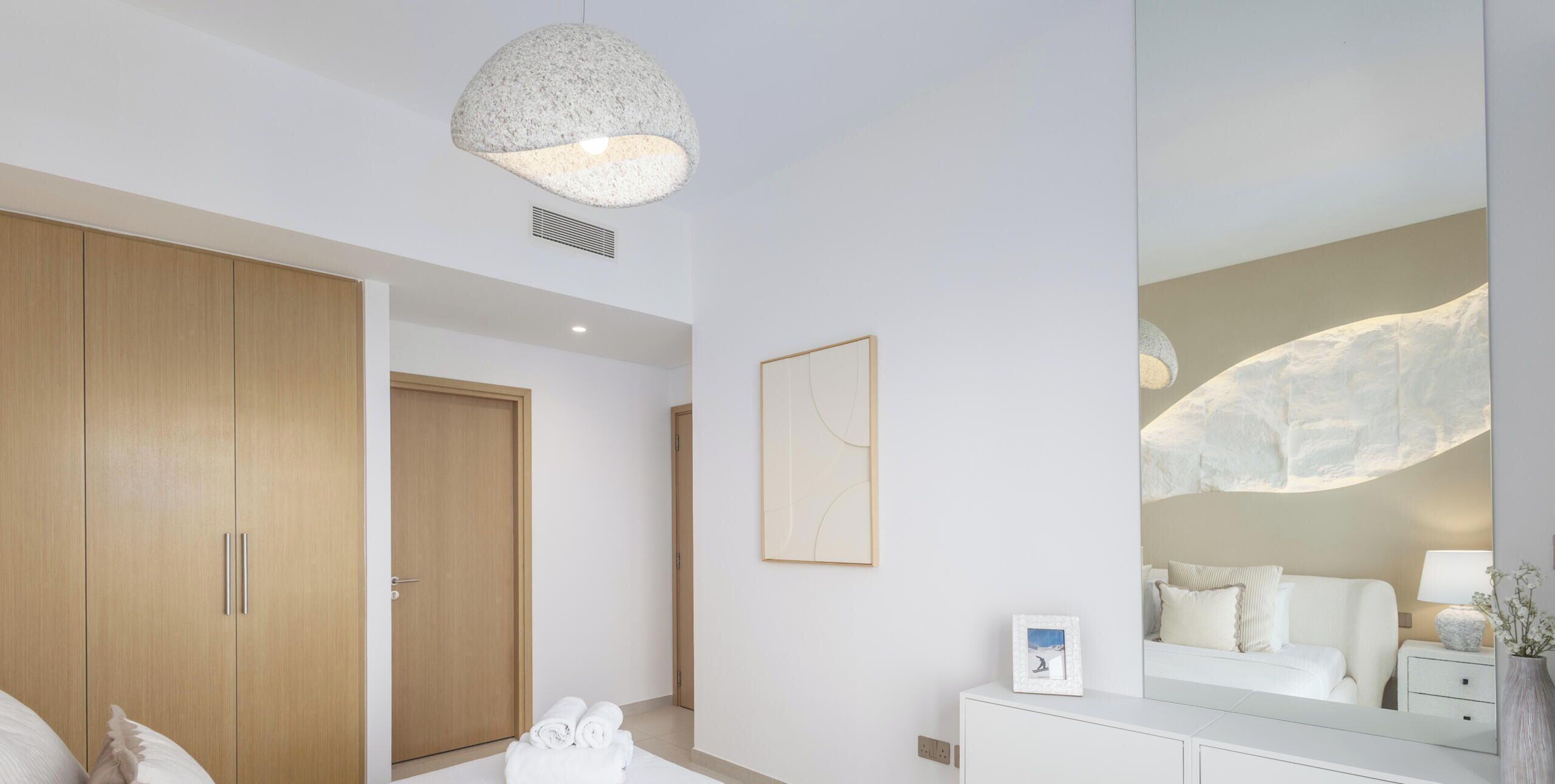 Una habitació d'hotel moderna amb un llit gran, un armari de fusta, un mirall i una làmpada penjant.