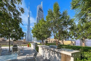 A rooftop terrace with outdoor seating, a view of the Burj Khalifa, and a sign for 'LUX HOLIDAY HOME'. - LUX | 47th Floor | Panoramic View | 2BR | Downtown (Dubai)