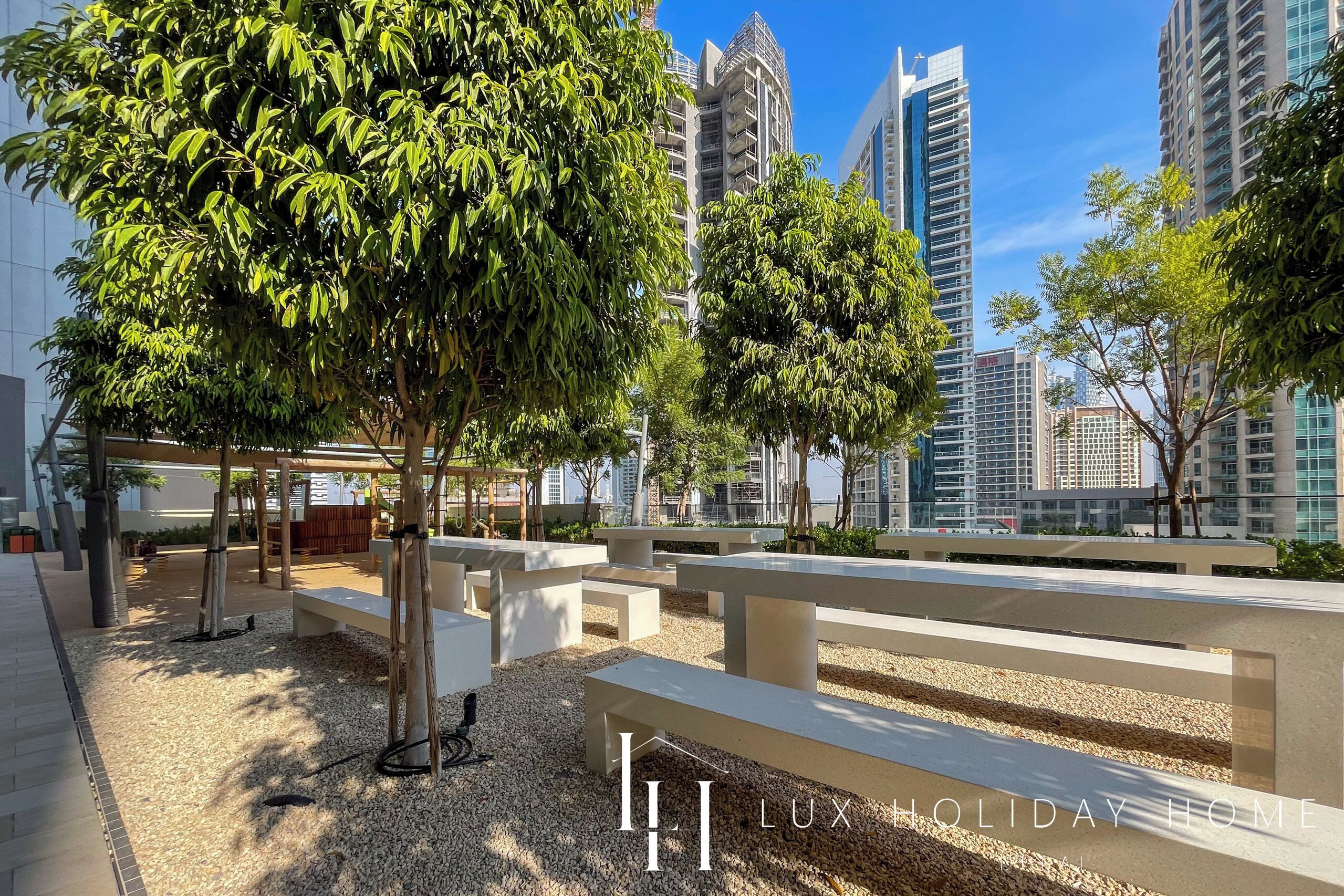 A modern outdoor area with benches and trees, surrounded by high-rise buildings.