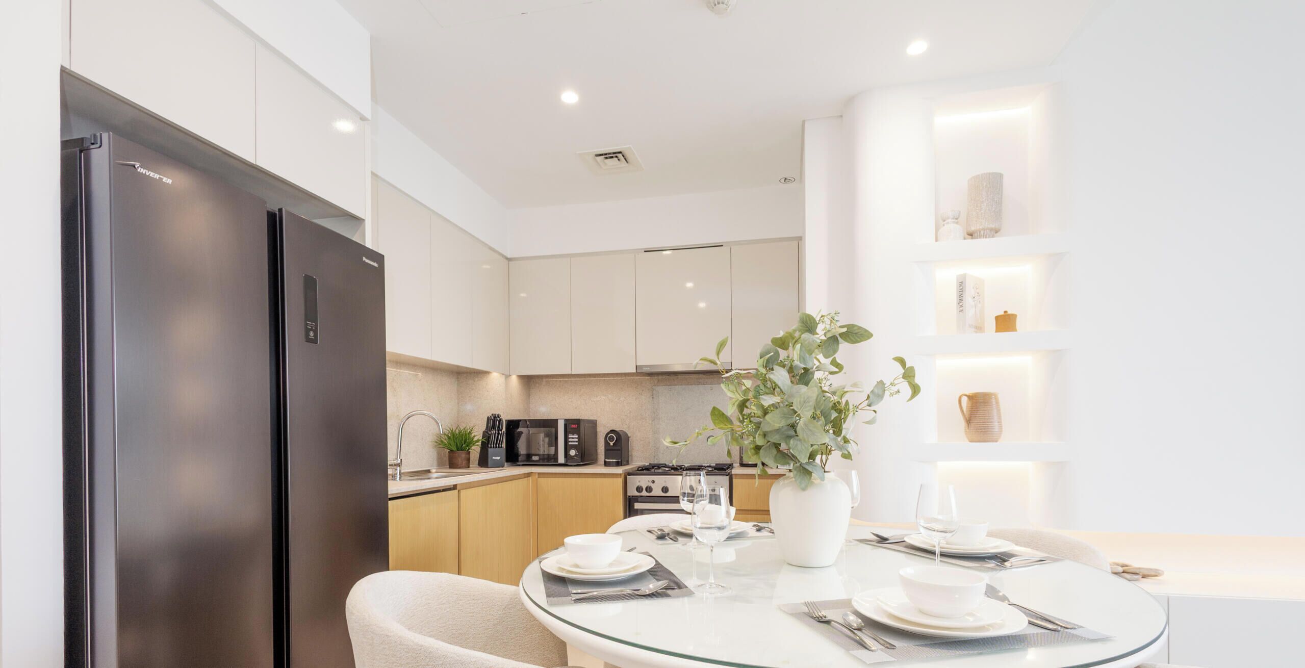 A modern kitchen with a black refrigerator, white cabinets, and a dining area with a glass table set for two.