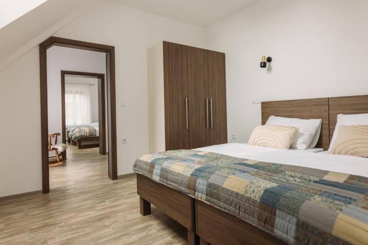 A bedroom with a wooden wardrobe, a bed with a patterned duvet, and a wooden floor.