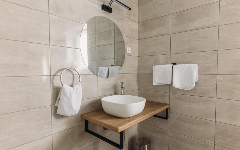 Un baño moderno con un espejo redondo, una encimera de madera y un lavabo blanco.