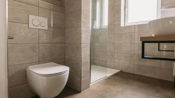 Un baño moderno con inodoro, cabina de ducha de vidrio y zona de lavamanos.