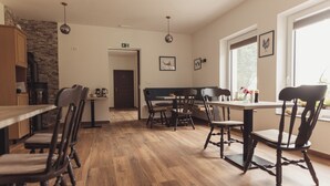 Un comedor con suelo de madera, una mesa central y sillas. Se ve una ventana con vistas a zonas verdes.