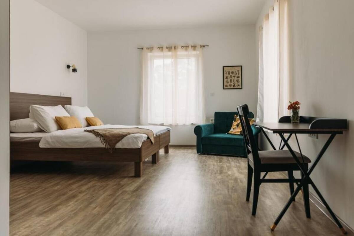 A bedroom with a bed, a desk, a chair, and a window with curtains.
