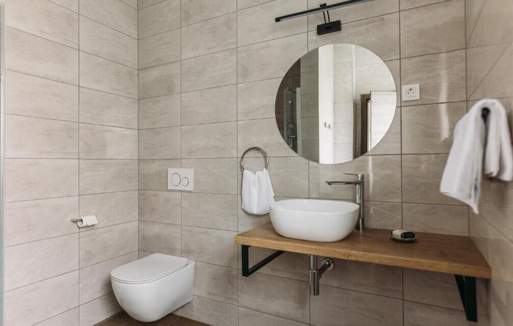 Un baño moderno con un espejo redondo, un lavamanos blanco y un inodoro.