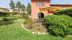 A building with a red facade, a yellow umbrella, and a garden with green shrubs and flowers. - Apartment Azzurro- Cignella Resort Tuscany (Trequanda)
